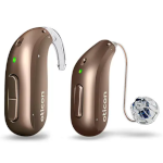 Two brown Oticon behind-the-ear hearing aids are shown, each with a small green indicator light; one has a clear tube, and the other has a thin wire leading to a dome-shaped earpiece.
